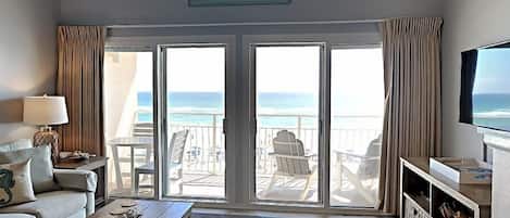 En inredning i ett hus vid stranden med en soffa, ett soffbord, en tv och utsikt över havet genom stora skjutdörrar.