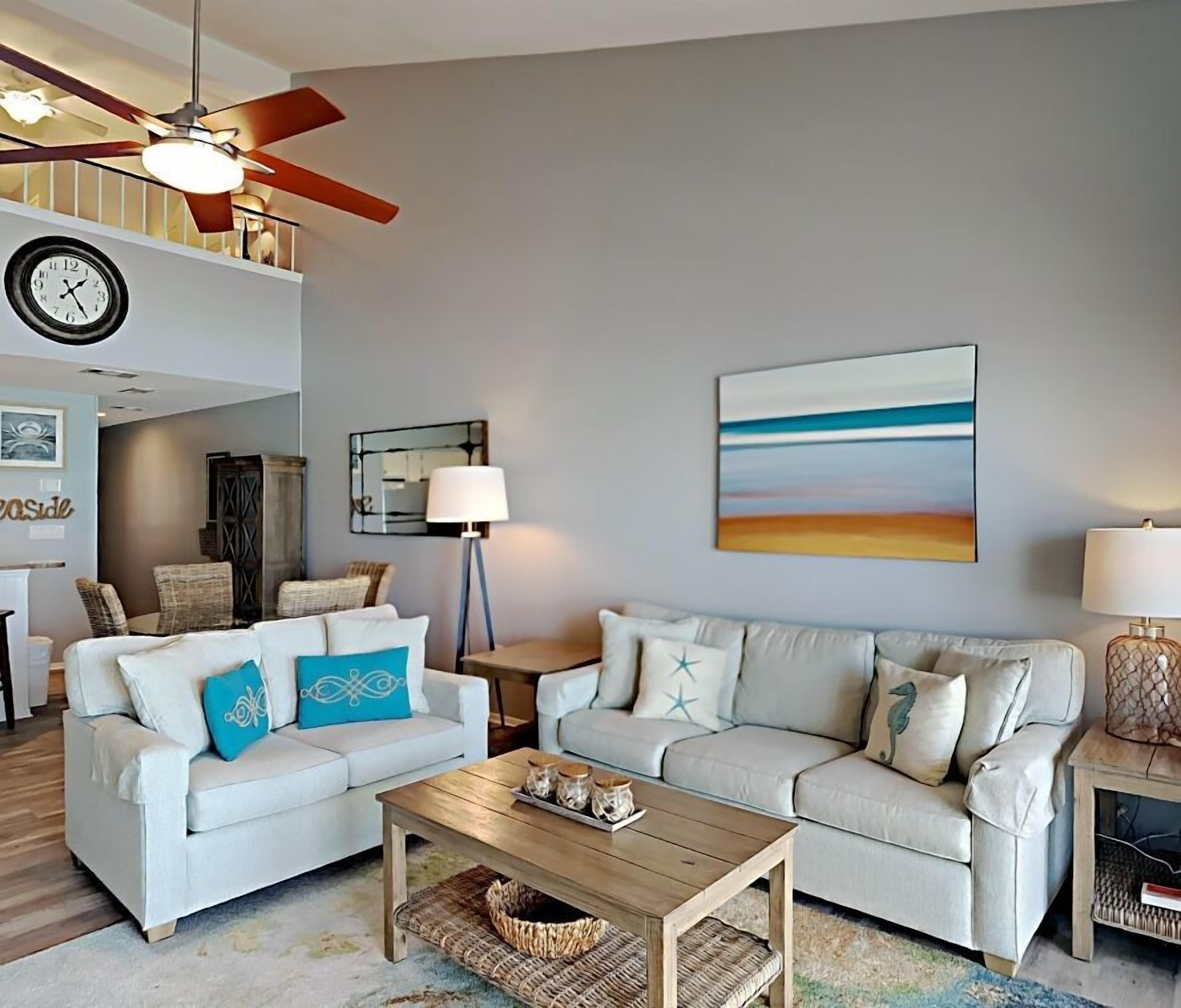 A living room with two white sofas, a wooden coffee table, a ceiling fan, a clock, and a painting on the wall.