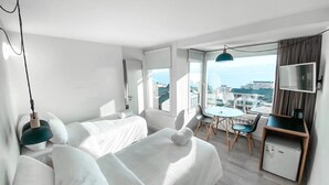 A modern hotel room with two beds, a small dining area, a TV, and a view of the city. - Hotel Patagonia Signature (San Carlos de Bariloche)