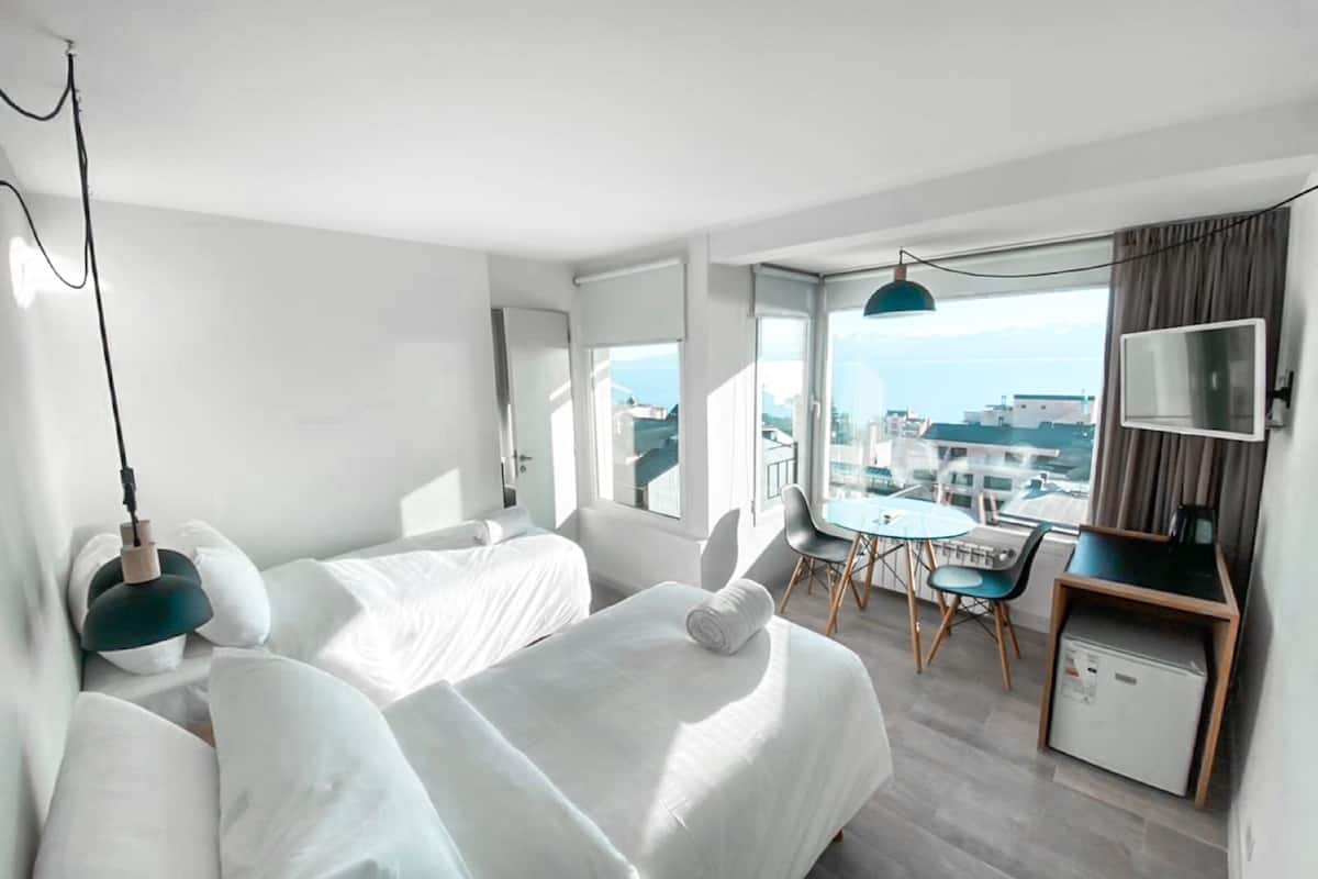 Ett modernt hotellrum med två sängar, en liten matplats, en TV och utsikt över staden.