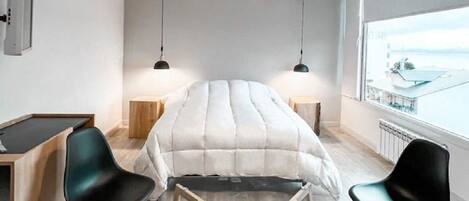 A modern hotel room with a large bed, two bedside tables, a desk, and chairs.