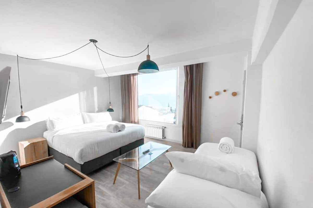Ett modernt hotellrum med en säng, en soffa, ett skrivbord och utsikt över staden.