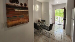 A dining area with a glass table and chairs, a painting on the wall, and a view of the outdoors. - Queen Angel Condo with Pool and Ocean View (Providenciales)