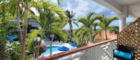 Un balcón con piscina, palmeras y vista a un edificio al fondo.