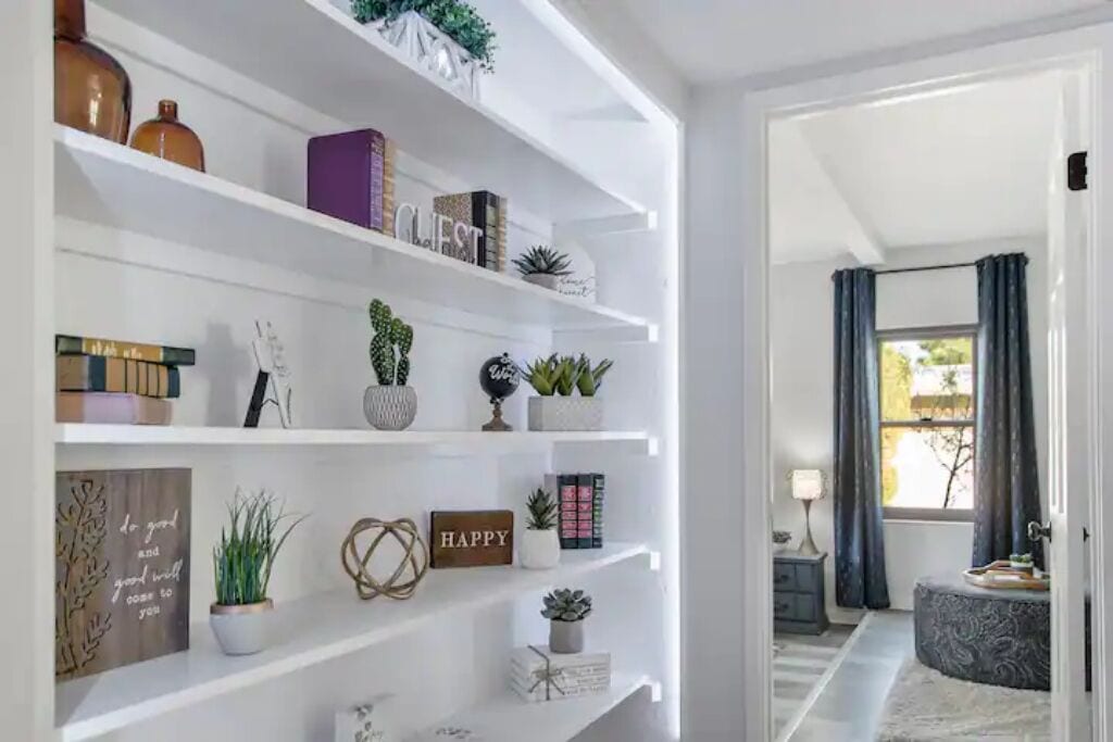 A modern living room with a white shelving unit displaying books, decorative items, and plants.