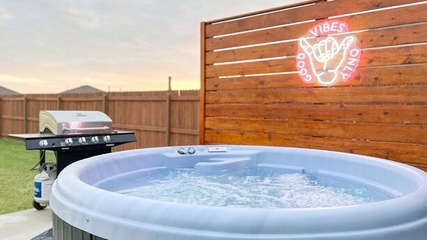 A hot tub with a wooden deck and a neon sign in the background.