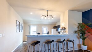 A modern kitchen with a central island, bar stools, and a potted plant.