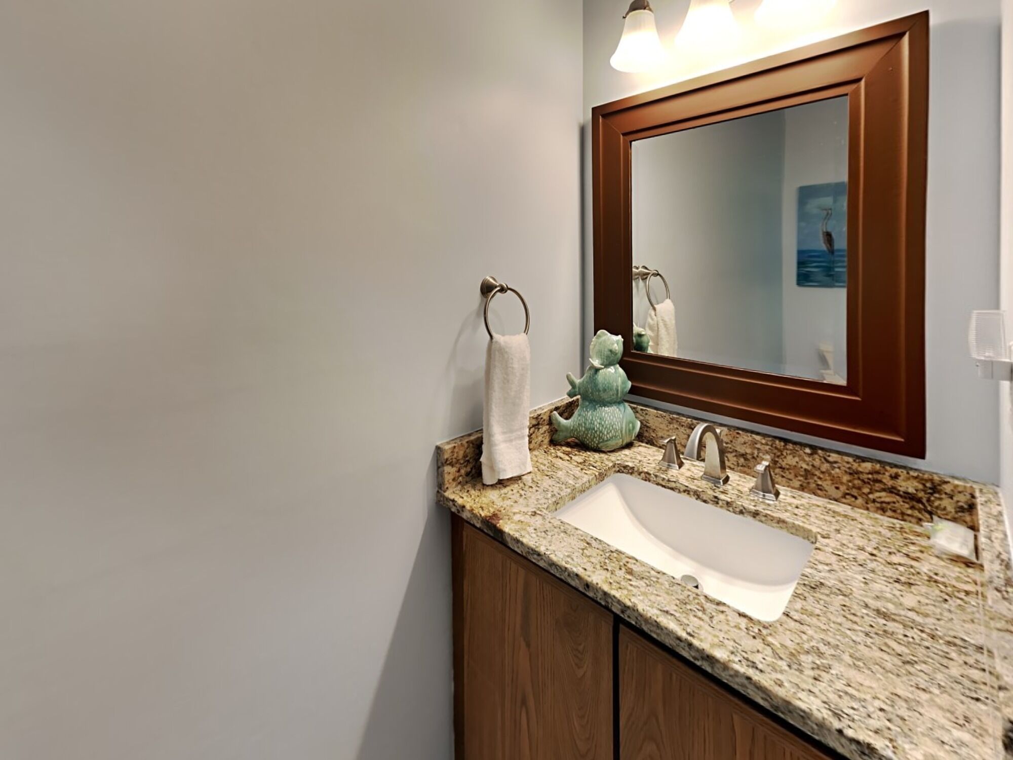 A bathroom with a granite countertop, a white sink, a wooden cabinet, a mirror with a wooden frame, and a towel rack with a white towel.