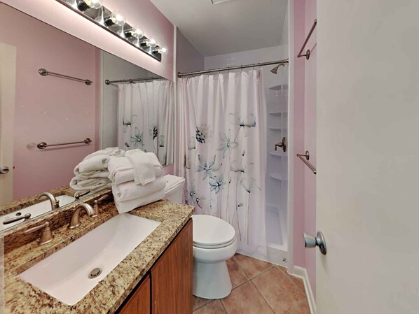 Une salle de bain équipée d’un meuble-lavabo, d’un évier, d’un miroir et d’un rideau de douche orné de motifs floraux.