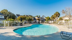 Piscina com cerca branca, espreguiçadeiras e posto de salva-vidas.