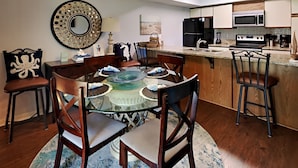 Uma cozinha compacta com eletrodomésticos modernos, uma área de refeições com mesa de vidro e um espelho decorativo.
