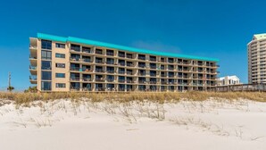 Un hotel de varios pisos con balcones, situado en una playa de arena.
