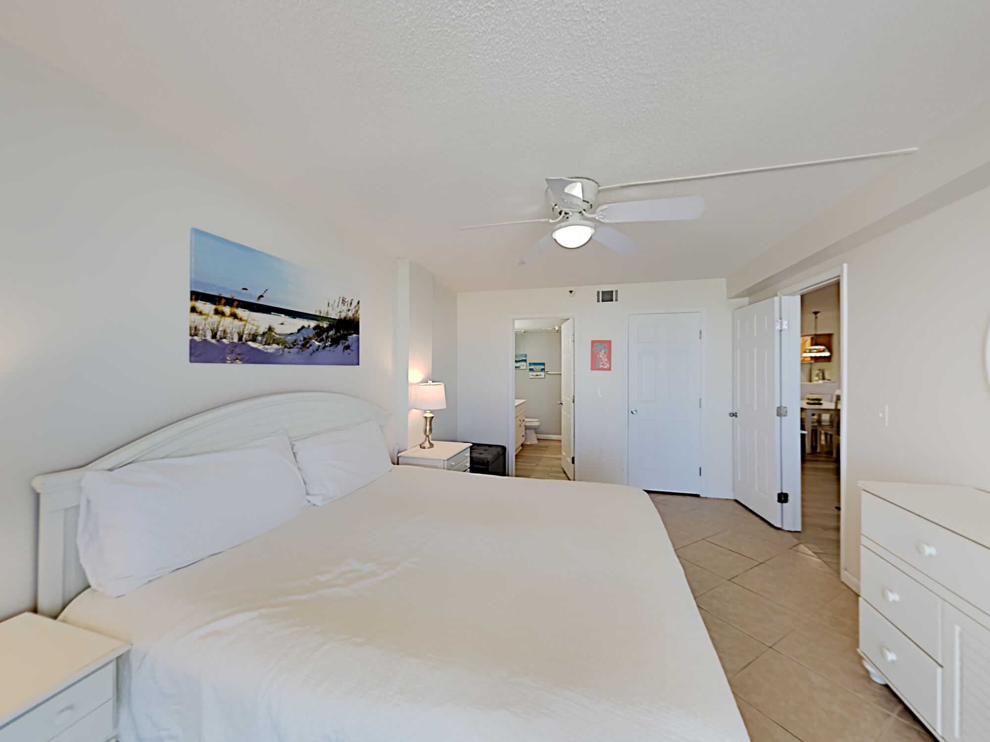 Une chambre à coucher avec un lit, une table de chevet, un ventilateur de plafond et un tableau accroché au mur.