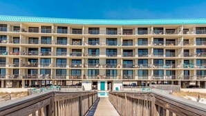 Un hotel de varios pisos con balcones, un paseo de madera y una zona de piscina.