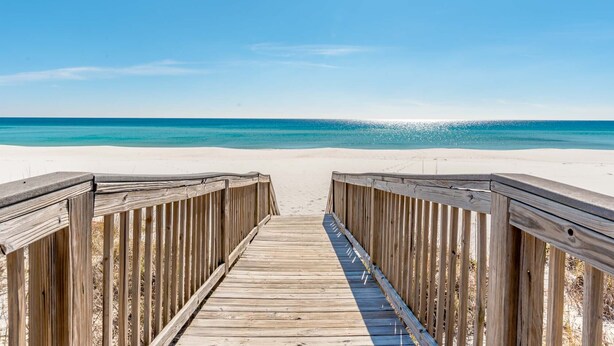 Un muelle de madera que conduce a una playa con aguas azules y transparentes.