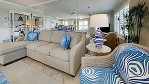 A spacious living room with a beige sectional sofa, a blue and white patterned armchair, and a small round table with a lamp. - Emerald Dunes #405 by Southern Vacation Rentals (Destin)