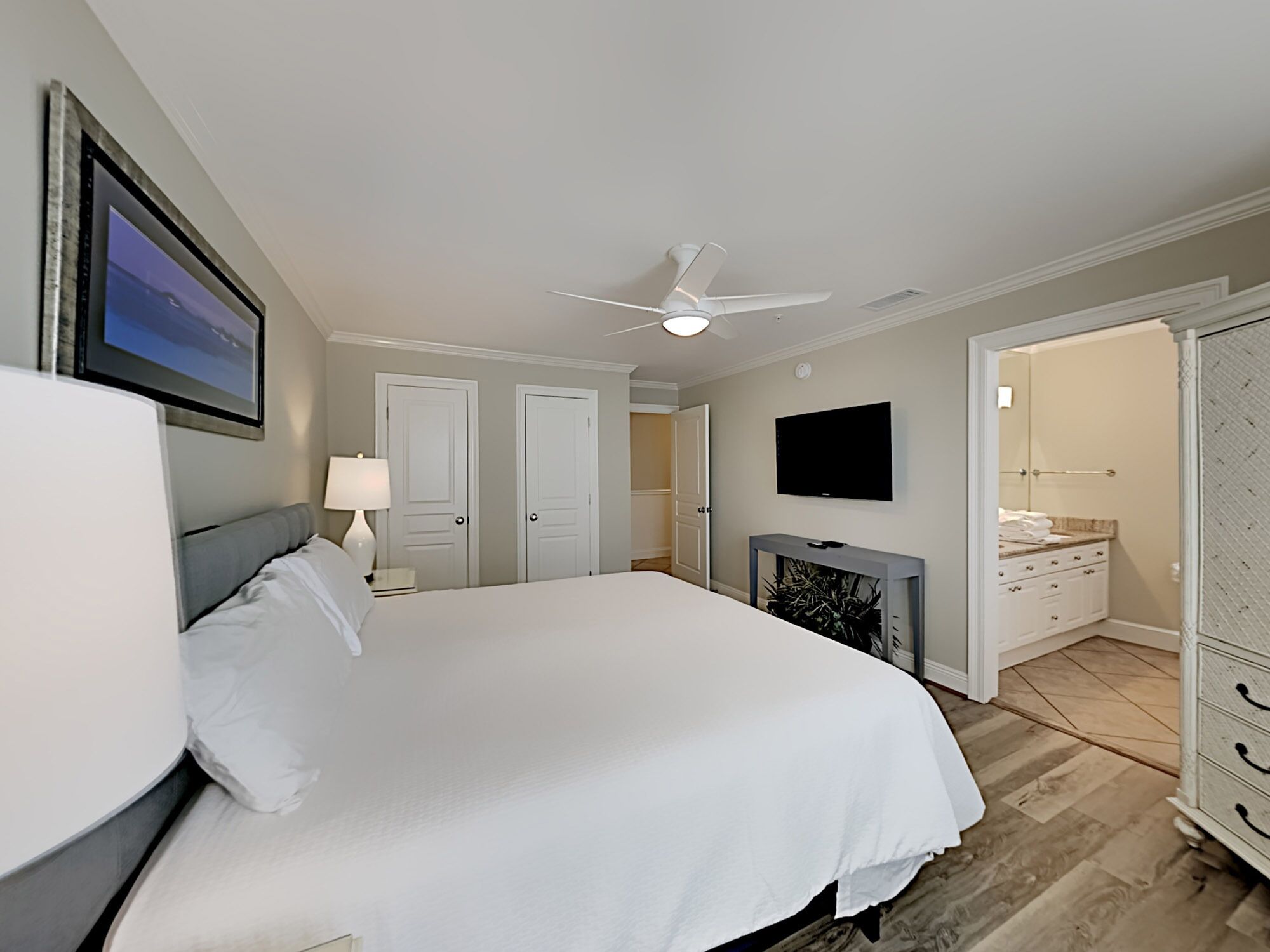 Ein Hotelzimmer mit einem großen Bett, einem Deckenventilator, einem Fernseher und einem durch eine offene Tür einsehbaren Badezimmer.