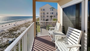A balcony with white chairs overlooking a beach and a building. - Emerald Dunes #405 by Southern Vacation Rentals (Destin)