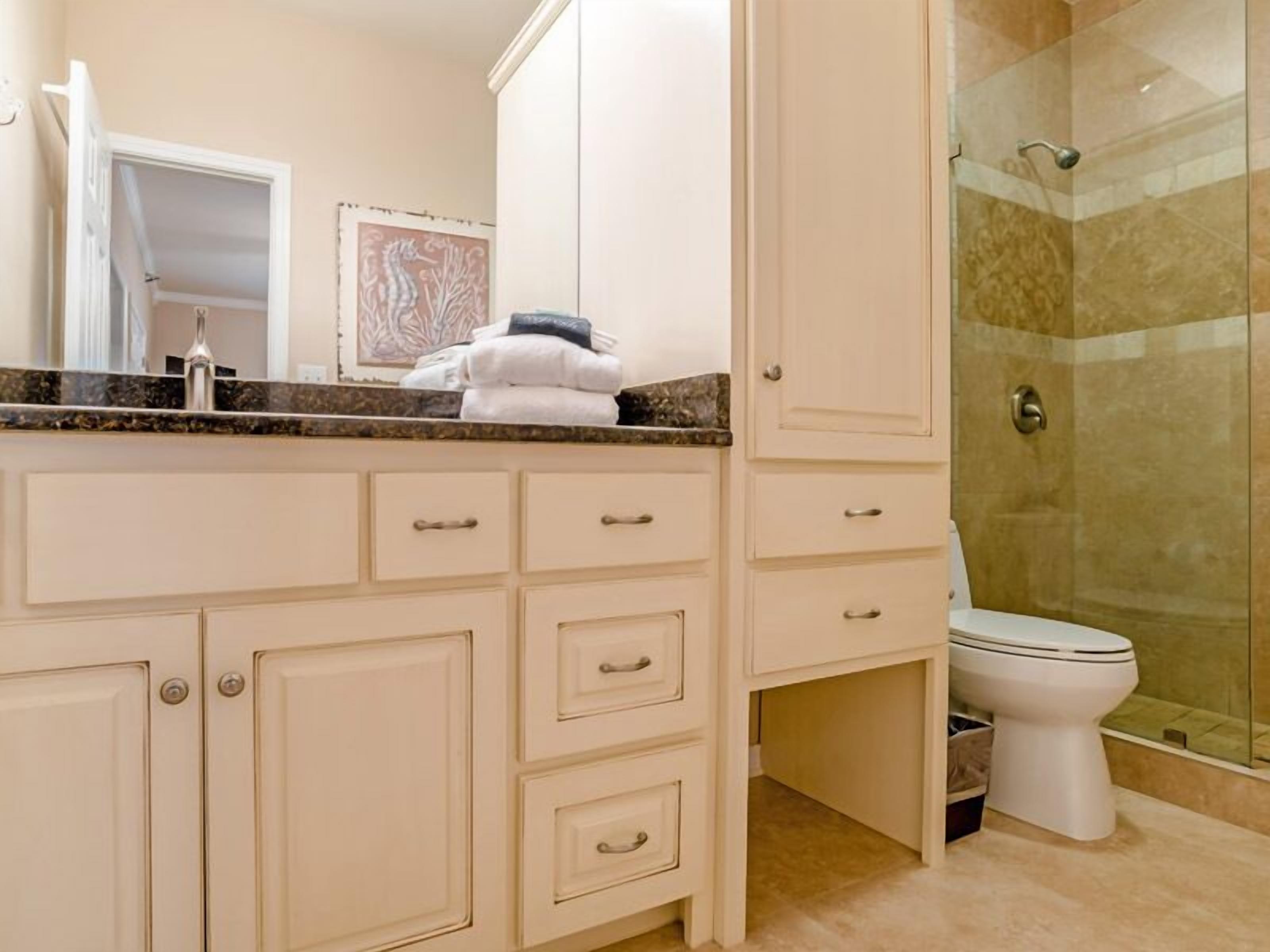 A bathroom with a marble countertop, a toilet, and a glass shower enclosure.