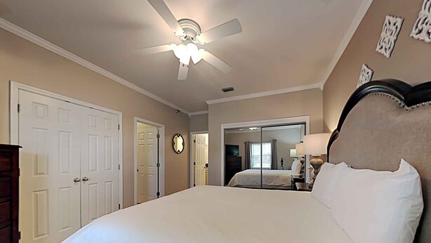 A bedroom with a large bed, a ceiling fan, a mirror, and a door.