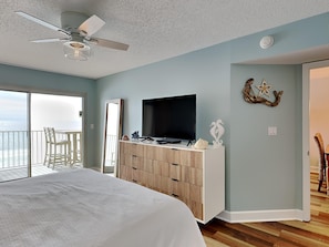 Relax in this serene bedroom with a large bed, ceiling fan, and flat-screen TV, plus a sliding door to a balcony with ocean views.