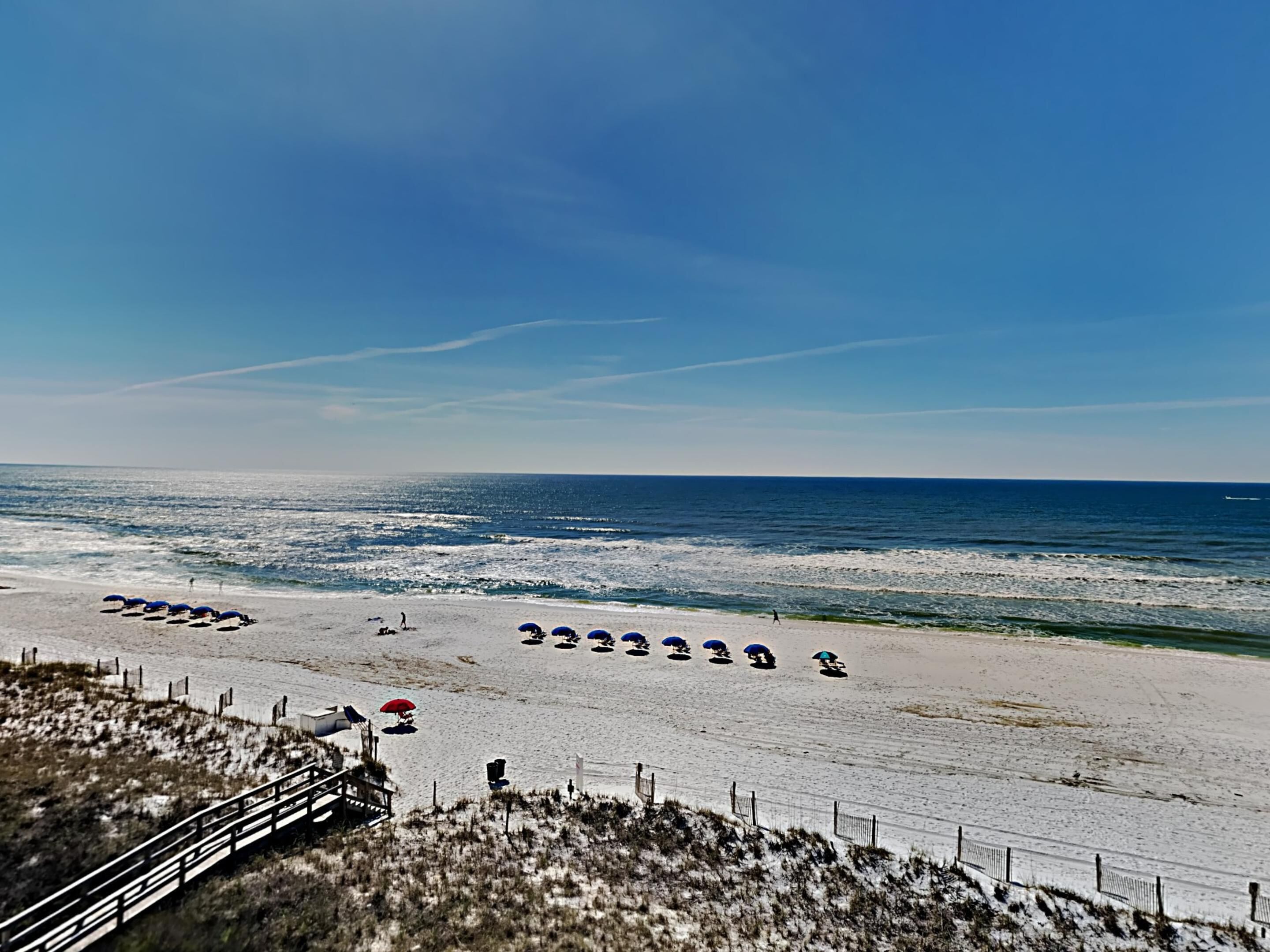 Een strand met parasols en een hek.