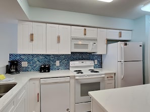 Kitchen area with white cabinetry, microwave, stove, oven, refrigerator, and coffee maker.