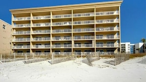 Een meerlaags hotel met balkons, gelegen aan een zandstrand.
