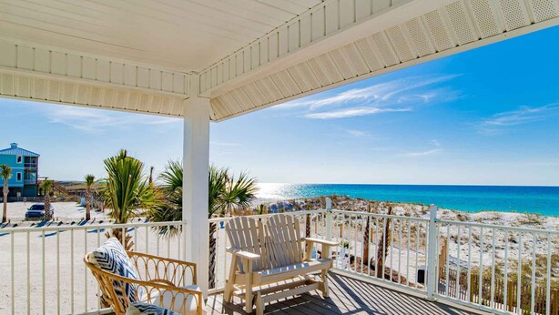 Eine Holzterrasse mit Korbstühlen und Blick auf Strand und Meer.