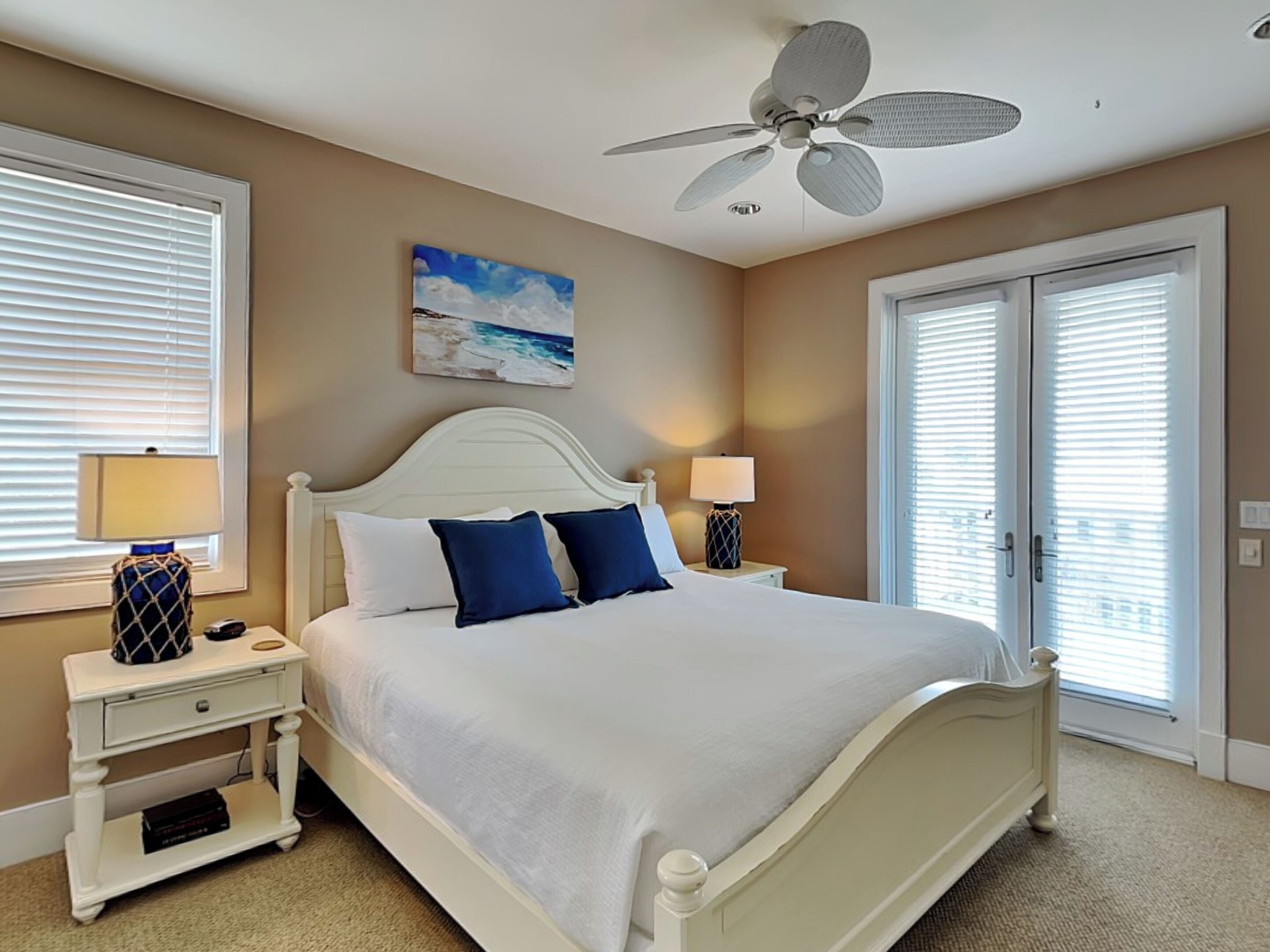 A bedroom with a bed, two bedside tables, a ceiling fan, and a painting on the wall.