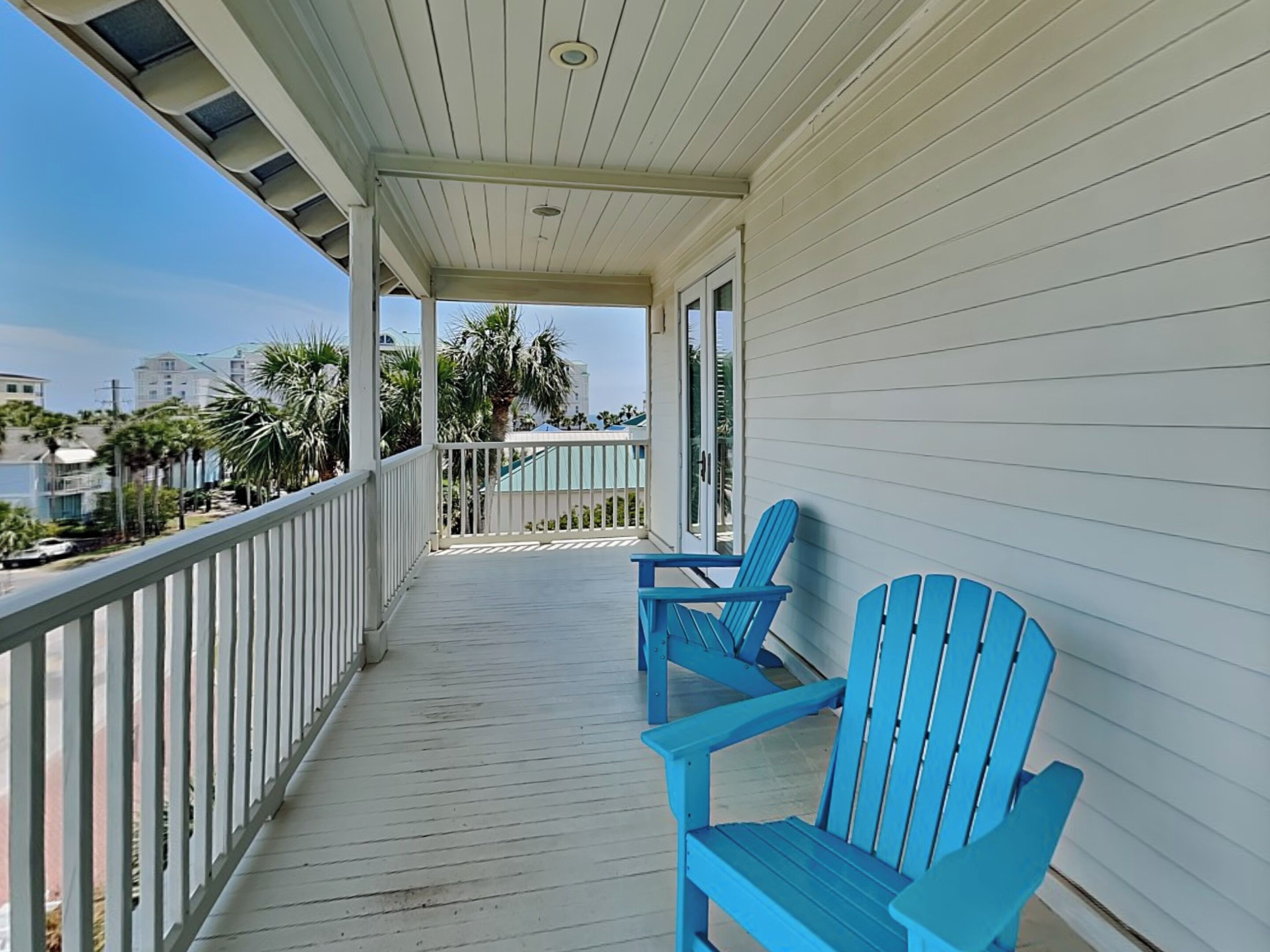 Un balcon abrité, doté de balustrades blanches et de chaises Adirondack bleues.