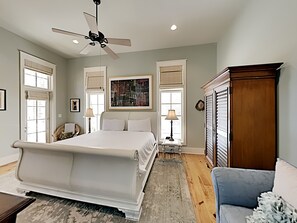 Une chambre à coucher avec un grand lit, un ventilateur de plafond, deux lampes de chevet, une armoire en bois et une fenêtre avec des stores.
