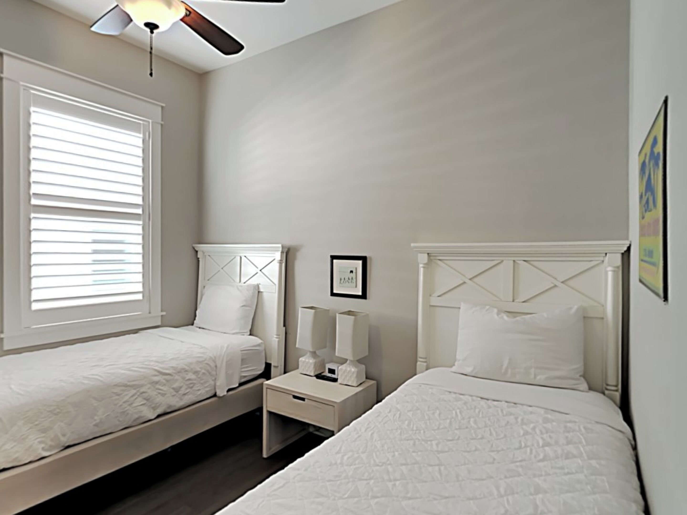 A bedroom with two single beds, a ceiling fan, a nightstand with a lamp, and a framed picture on the wall.