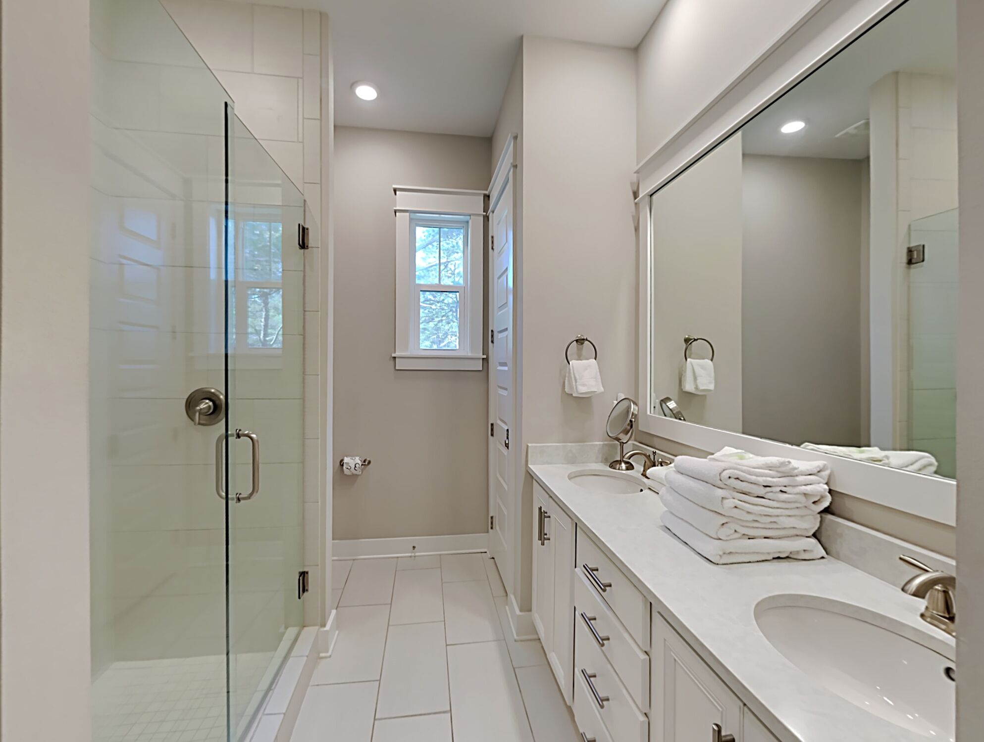 A modern bathroom with a glass shower enclosure, a large mirror, and a vanity with a sink and towel stack.