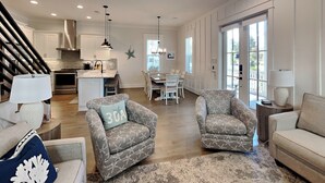 A spacious living room with two armchairs, a sofa, a dining area, and a kitchen. - Starfish Sanctuary by Southern Vacation Rentals (Santa Rosa Beach)