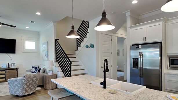 A modern kitchen with a large island, stainless steel appliances, and a staircase with black railings. - Starfish Sanctuary by Southern Vacation Rentals (Santa Rosa Beach)
