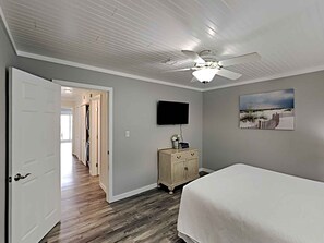 Une chambre à coucher avec un lit, un ventilateur de plafond, une télévision et un tableau accroché au mur.