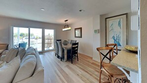Una sala de estar moderna con un sofá, una mesa de comedor y sillas. Una ventana grande proporciona luz natural y vistas al exterior.
