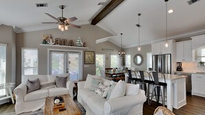 A spacious living room with a large sofa, a coffee table, and a dining area with a kitchen in the background. - The Taj Mahal by Southern Vacation Rentals (Santa Rosa Beach)