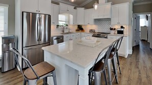 A modern kitchen with white cabinetry, stainless steel appliances, and a large island with bar stools. - The Taj Mahal by Southern Vacation Rentals (Santa Rosa Beach)