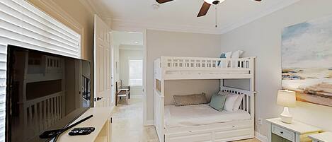 A bedroom with a bunk bed, a television, and a ceiling fan.