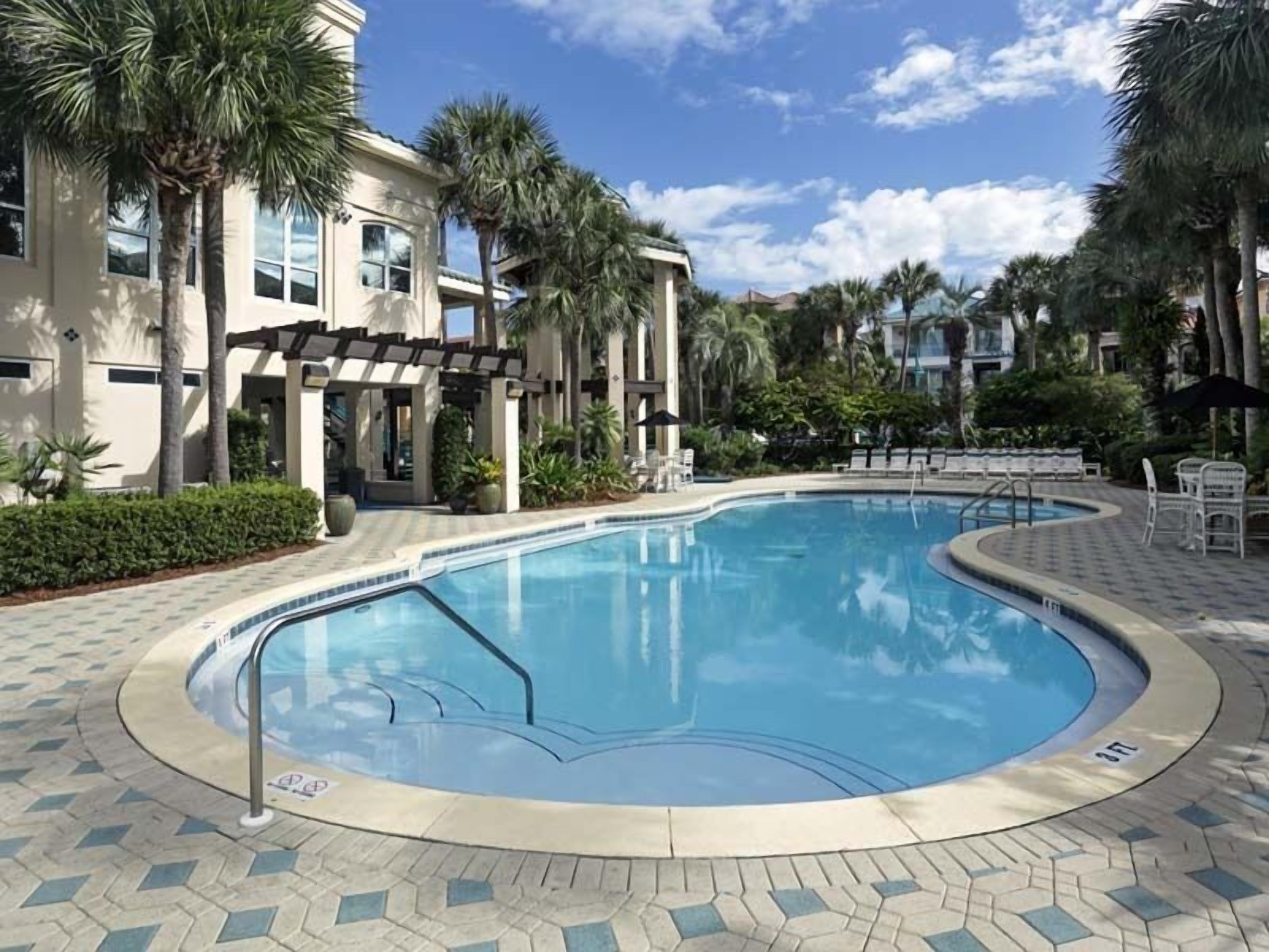 Una piscina con solárium empedrado, palmeras y un edificio con columnas.