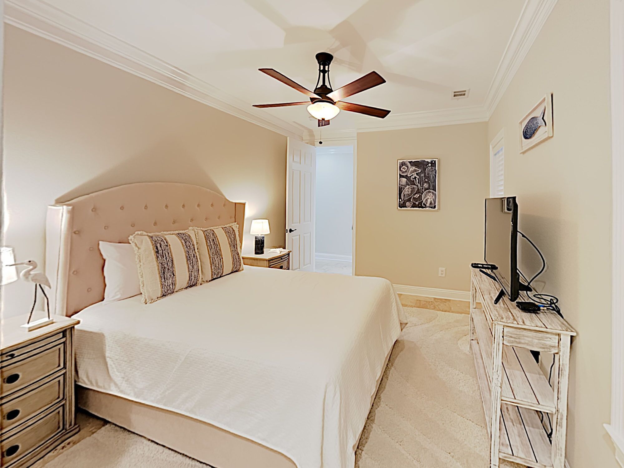 A bedroom with a large bed, a ceiling fan, a nightstand, a dresser, and a television.