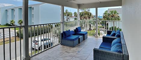 A covered balcony with wicker furniture and a view of a residential area.