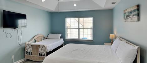 A bedroom with a bed, a chair, a television, and a ceiling fan.