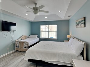 Un dormitorio con cama, una silla, un televisor y un ventilador de techo.