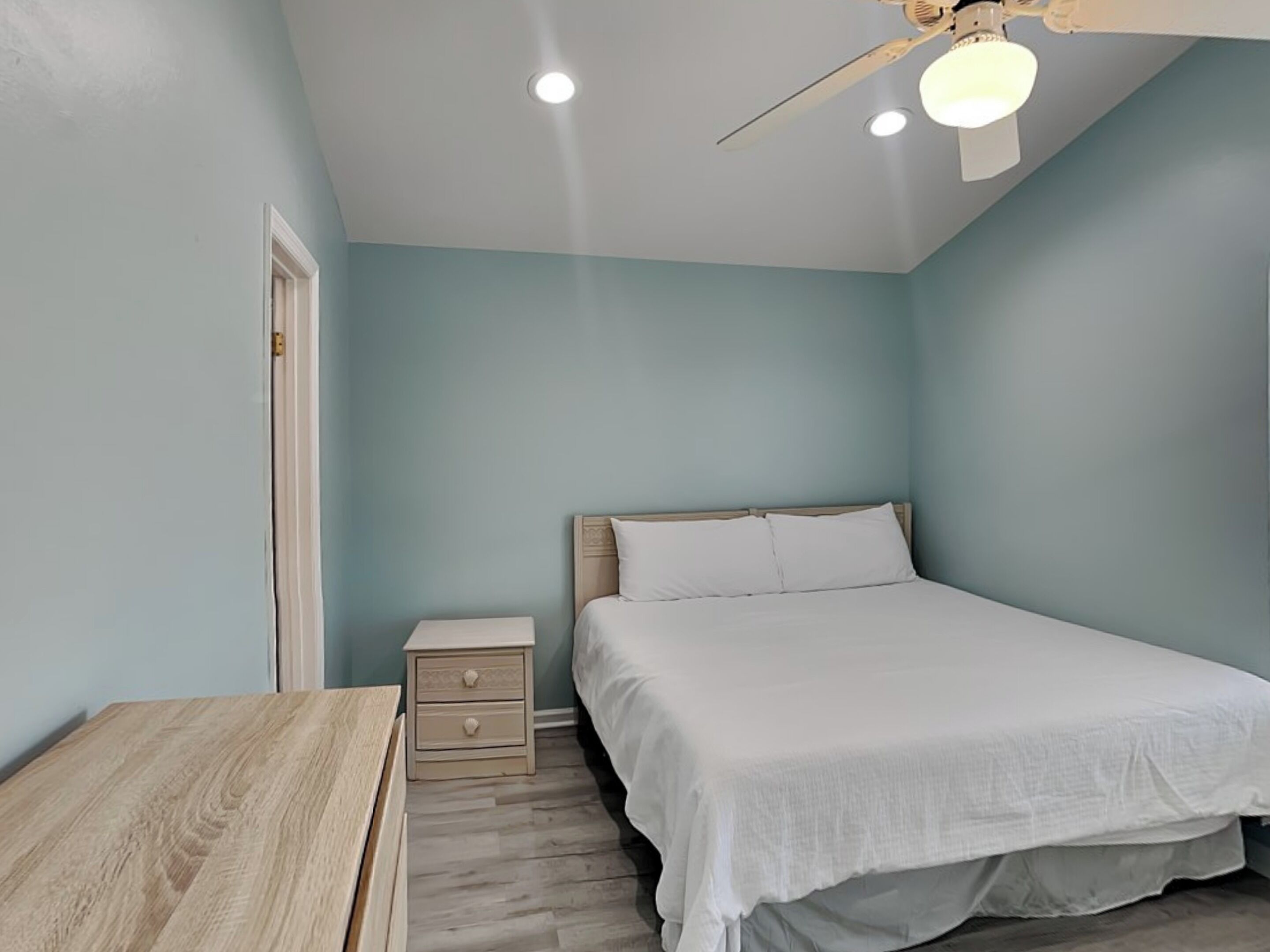 Un dormitorio con cama, mesita de noche, mesa de madera y ventilador de techo.
