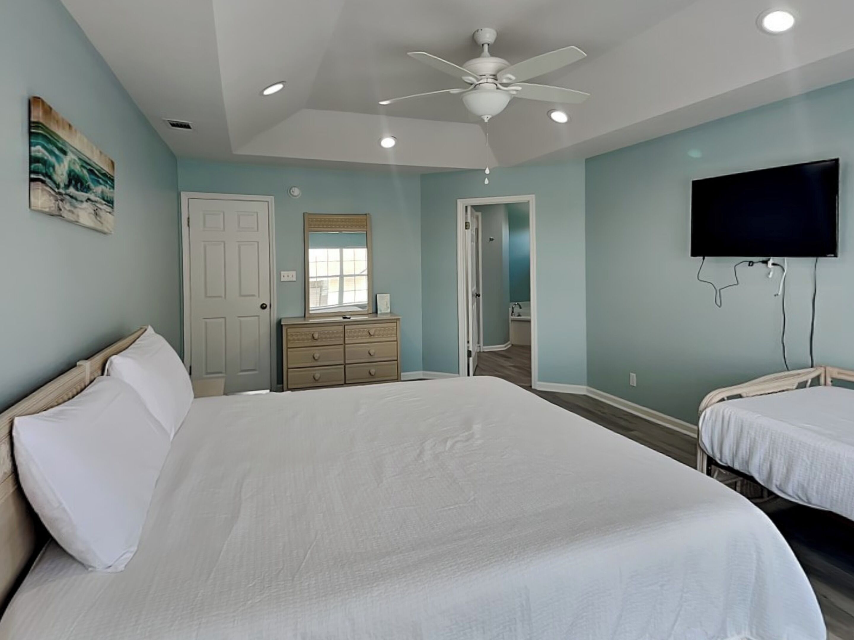 A bedroom with a large bed, a dresser, a television, and a ceiling fan.