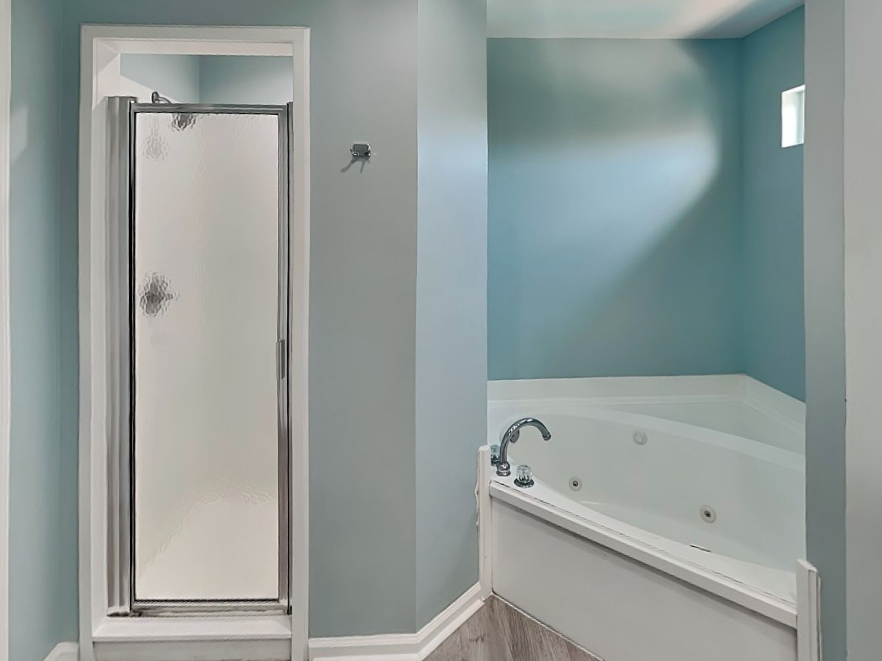 Un baño con mampara de vidrio, bañera y paredes azul claro.