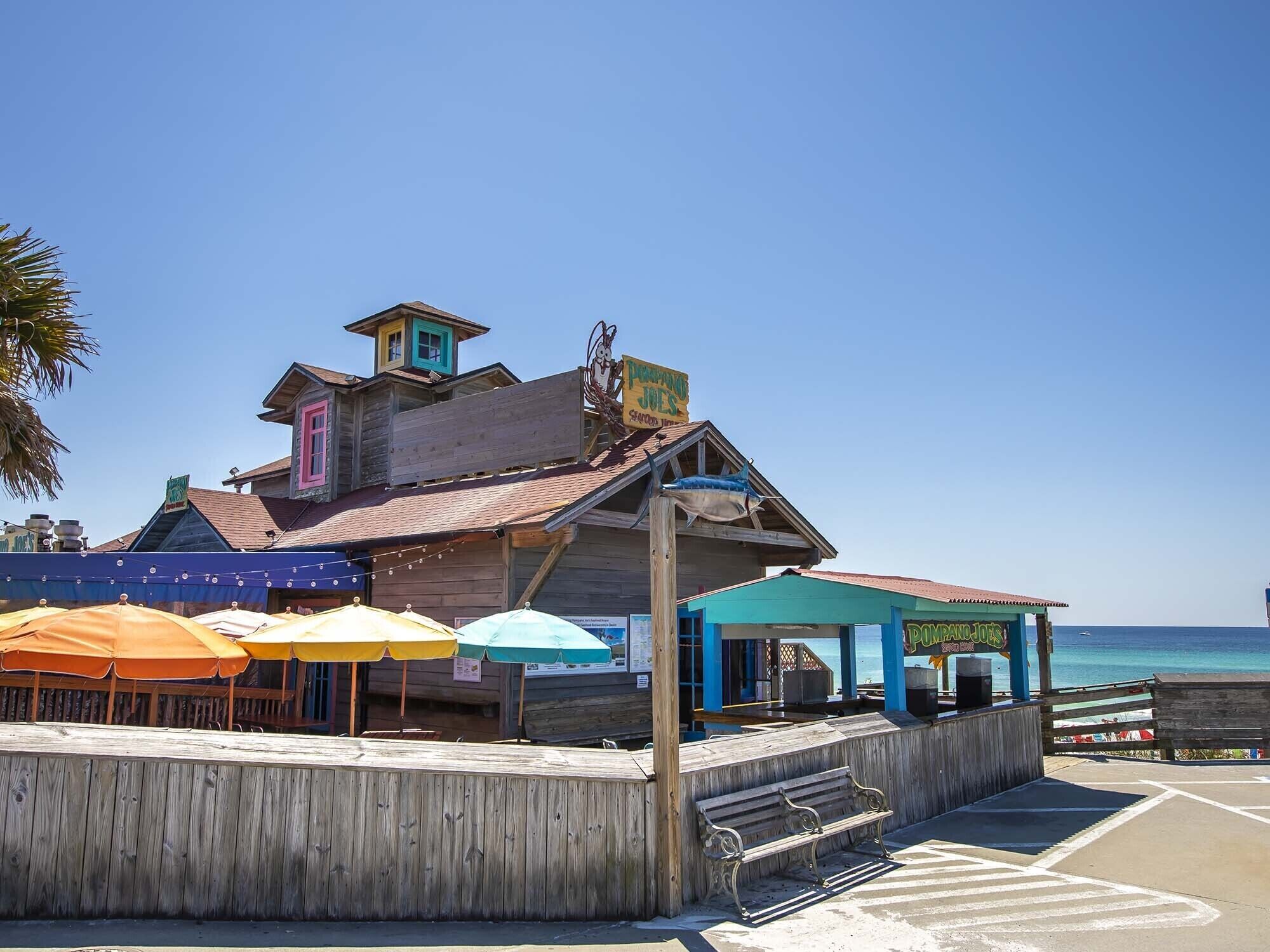 A wooden building with a blue roof and a sign that reads "Dolphin Lodge." There are colorful umbrellas and a wooden bench outside.